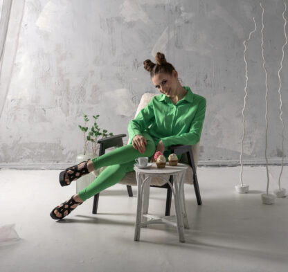 Cute girl smiles and drinks coffee with cupcakes in studio. Young woman in green suit poses on gray background.